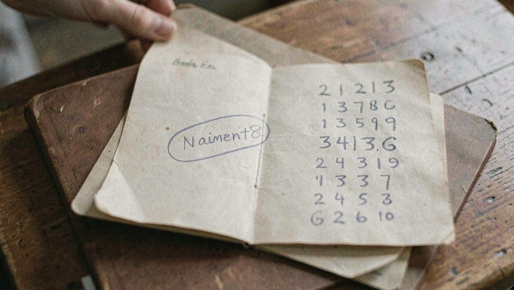 Carnet de famille ouvert sur une table avec une date de naissance entourée au crayon et des chiffres tracés en colonne à côté